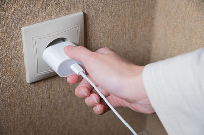 Female hand turns on or off the smartphone charger from the socket on the wall, white color