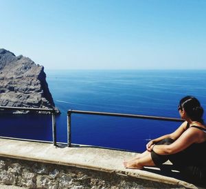 Woman standing on retaining wall by sea against clear sky