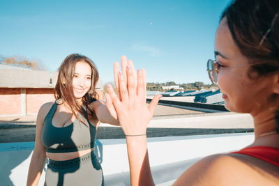 Side view of young woman with arms raised against sky