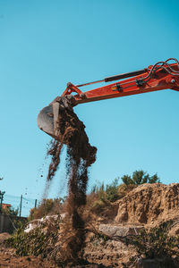 Low angle view of crane at construction site against clear blue sky