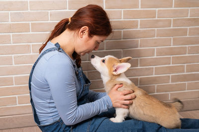 Woman embracing puppy against wall