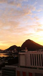 Silhouette buildings by mountains against sky during sunset