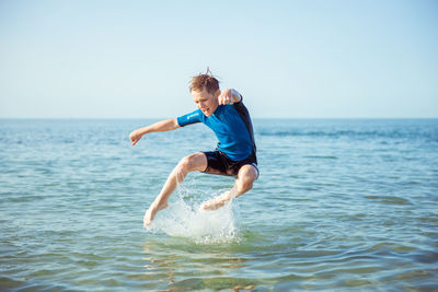 Full length of boy jumping in sea water against sky