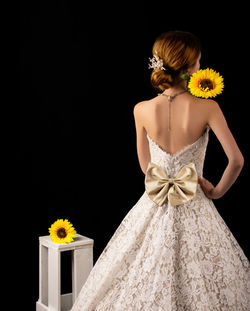 Rear view of woman holding yellow flower against black background