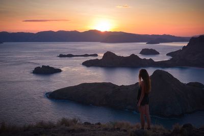 Rear view of woman standing on shore against sunset sky