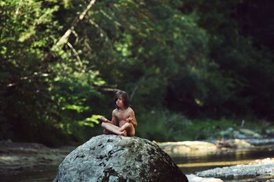 Boy sitting on stone by water