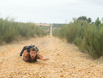 Portrait of young man lying on dirt road against sky