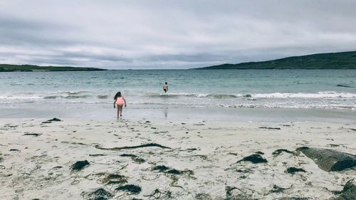 Rear view of people on shore at beach against sky