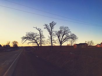 Bare trees on landscape against clear sky