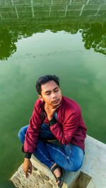 High angle view of young man sitting by lake