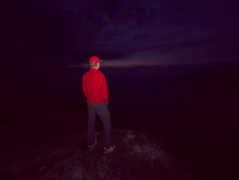 Man lost in thick mist rocks waiting for daybreak. big adventure in wild nature. hiker in red hoodie