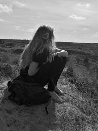 Woman sitting on field against sky