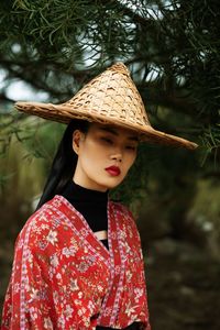 Portrait of young woman wearing hat standing against plants