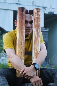 Young man embracing rusty metal while sitting outdoors