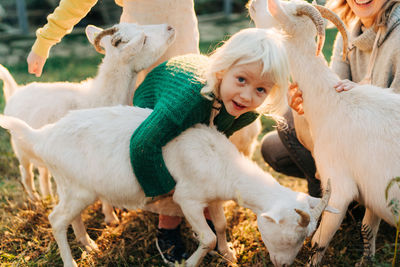 Little adorable empathic blonde girl hugs a white goat on the farm.