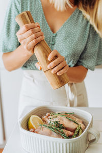 Caucasian woman with a pepper grinder seasoning raw chicken with herbs