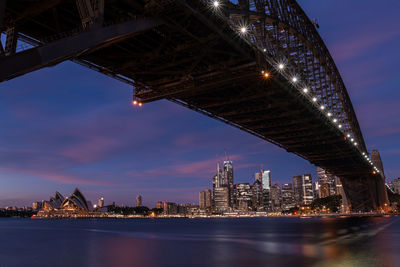 Sydney harbor bridge over river in illuminated city against sky at night