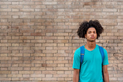 Portrait of young man standing against brick wall