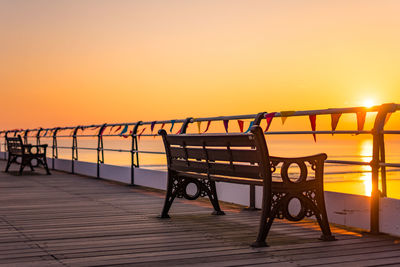 Empty bench against orange sky during sunset