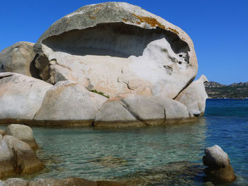 Rock formation in sea against clear blue sky