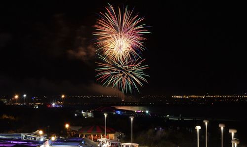 Firework display over illuminated city against sky at night