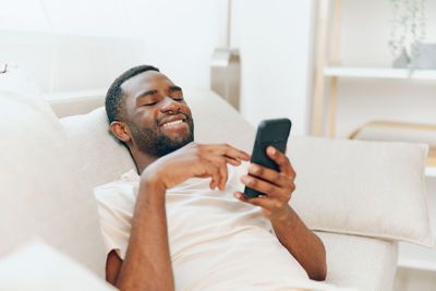 Young woman using mobile phone while sitting on bed at home