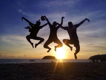 Low angle view of silhouette man jumping at beach against sky during sunset