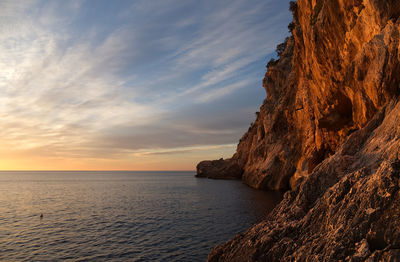 Rock formation in sea against sky during sunset