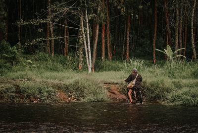 Rear view of man riding bicycle in river against forest
