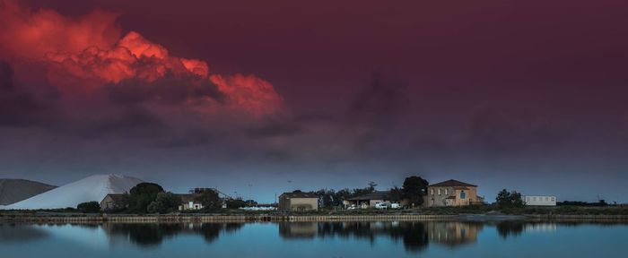 Scenic view of lake by buildings against sky at sunset