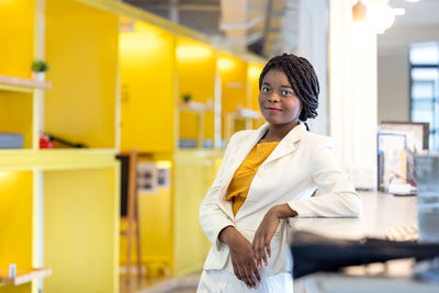 Portrait black woman in modern office in coworking background, afro woman in yellow sweater