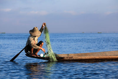 Fisherman holding net on boat in sea against sky