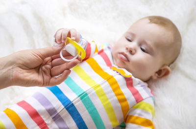 Mother holding pacifier while baby lying on bed