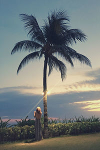 Woman by palm tree against sky during sunset