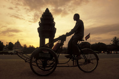 Man riding bicycle against sky during sunset