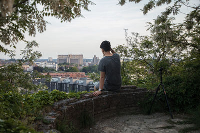 Man sitting on retaining wall amidst trees in city