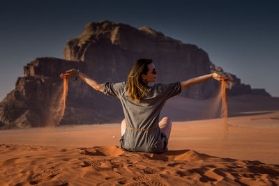 Rear view of woman with arms raised on desert against sky