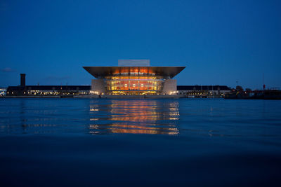 Illuminated building by sea against blue sky