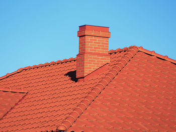 Red roof tiles with red brick chimney on blue sky background.