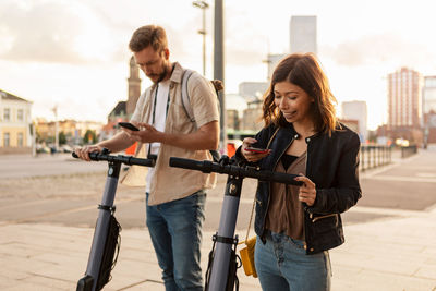 Male and female commuters scanning through mobile phone while unlocking electric push scooters in city