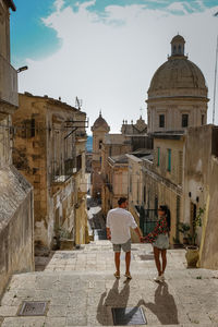 Rear view of people walking by buildings in city