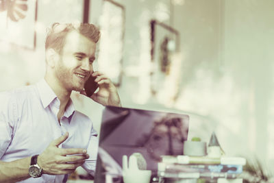 Smiling businessman using phone and laptop while sitting in office