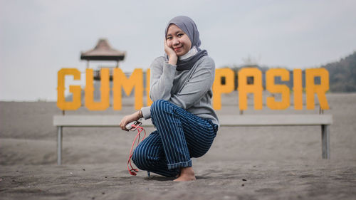 Portrait of smiling young woman by text on sand