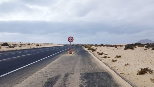 Road sign in desert against sky