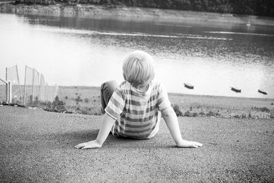 Rear view of boy sitting at lakeshore