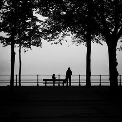 Silhouette mother and daughter by trees against sky