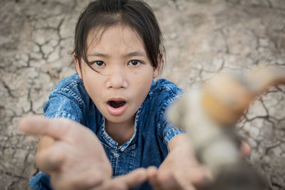 High angle view of girl sitting with hands cupped on cracked field