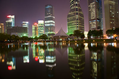 Illuminated buildings by lake against sky in city at night