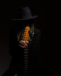 Female model wearing hat while holding guitar against black background