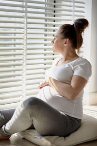 Side view of woman sitting on bed at home